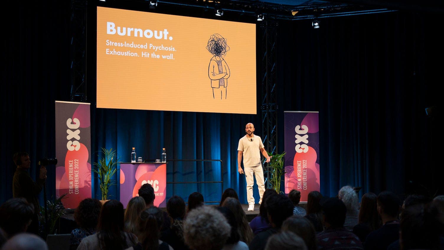 Anik Devaughn on stage at the STHLM Xperience Conference (SXC) 2022, presenting a slide titled Burnout.